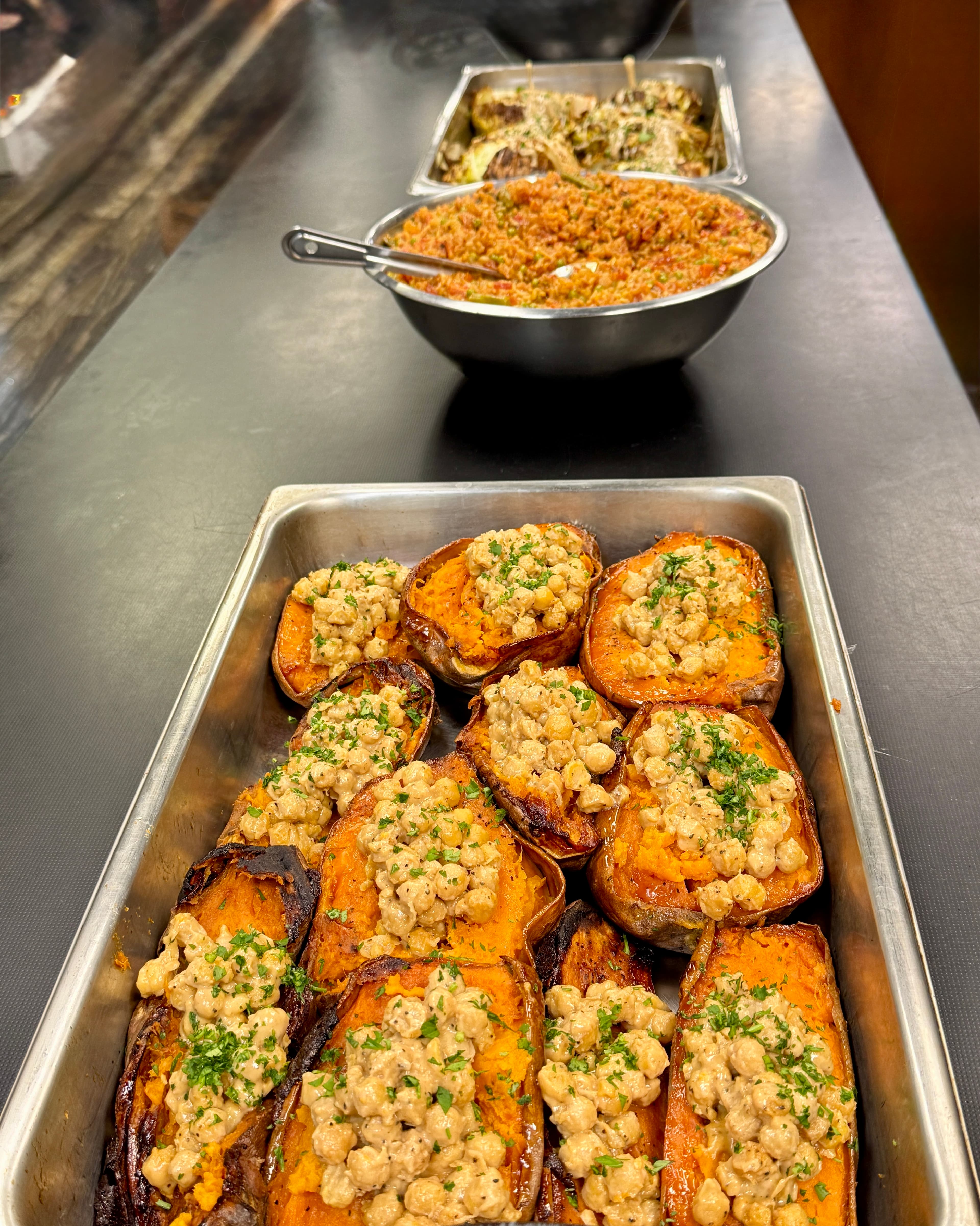 Roasted sweet potato halves topped with creamy chickpeas and parsley in a metal tray.