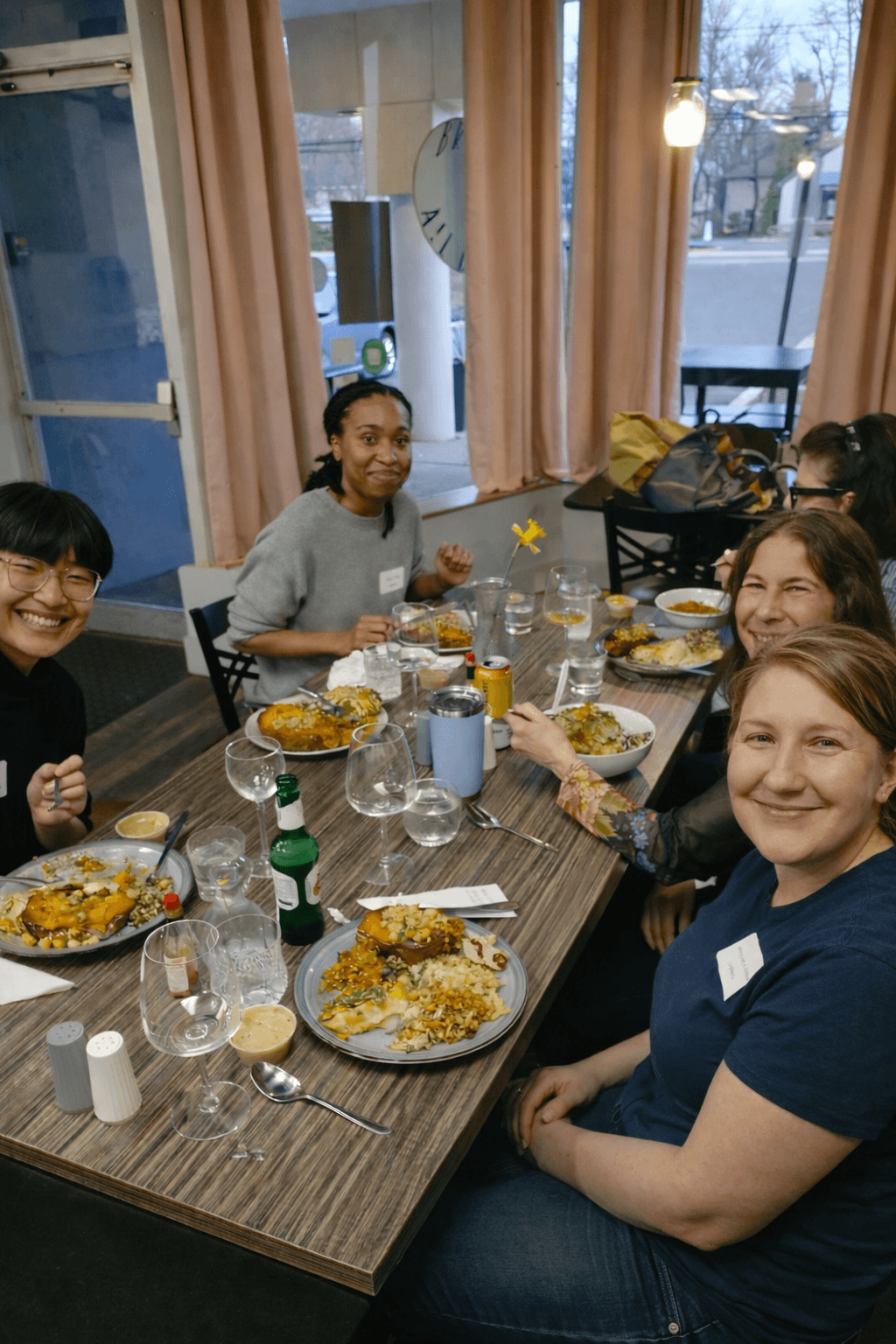 Smiling women gathered around a long wooden table enjoying a meal together in a restaurant.
