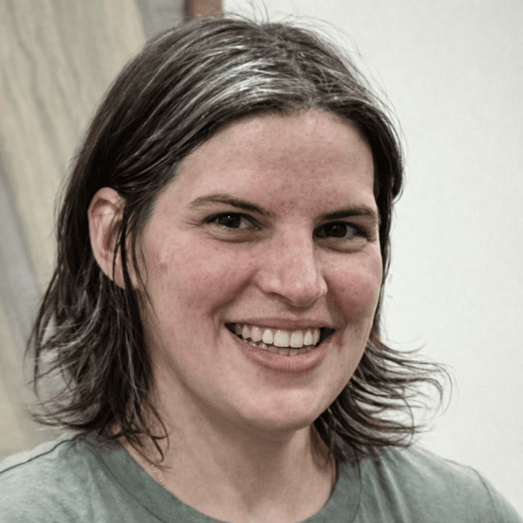 Smiling woman with dark, grey-streaked hair wearing a green t-shirt in a close-up portrait.