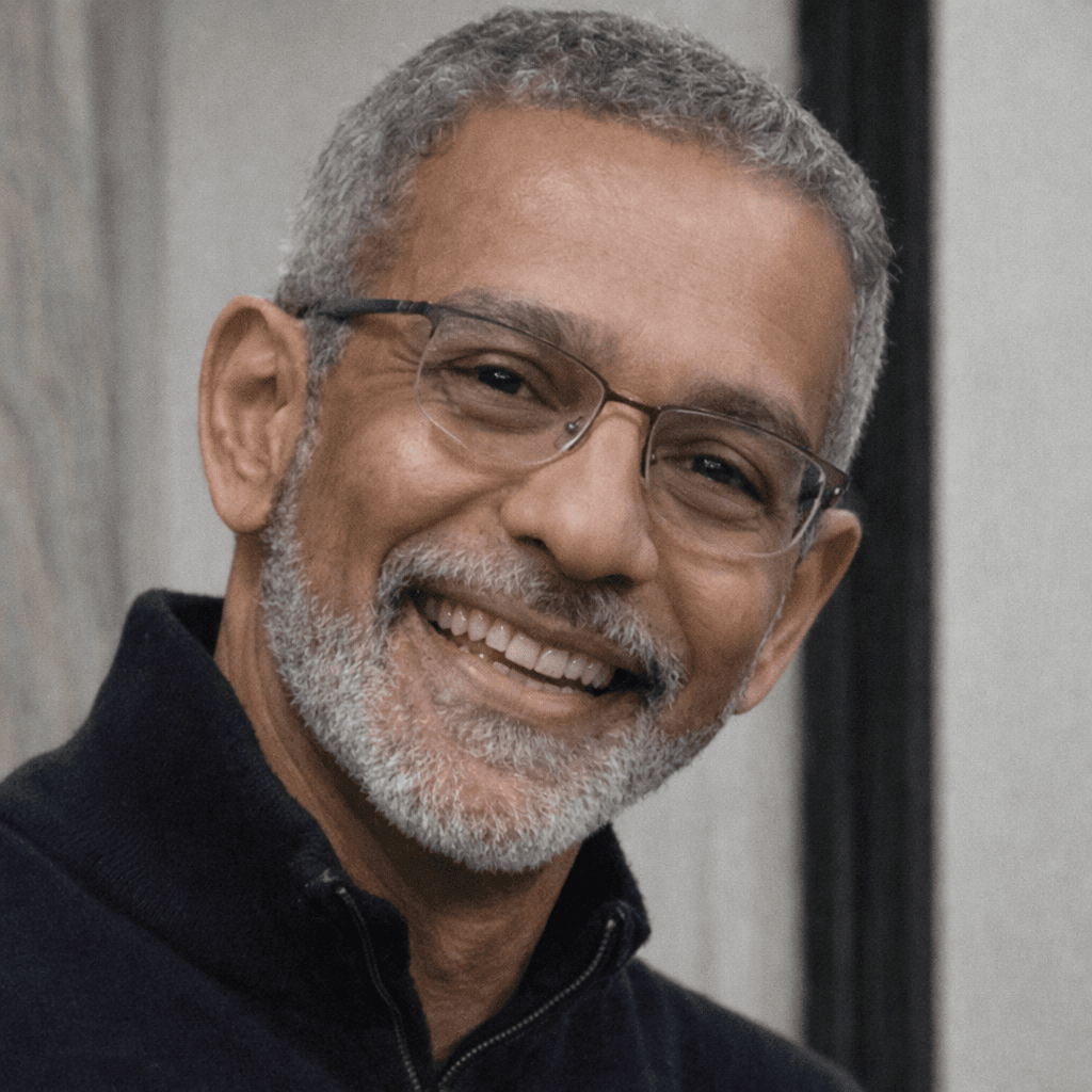 Smiling middle-aged man with salt-and-pepper hair, beard, and glasses wearing a dark blue sweater.